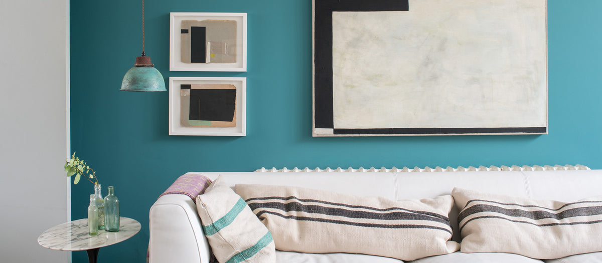 Ein Wohnzimmer mit einer türkisen Wand, davor ein weißes Sofa und schwarz graue Bilder an der Wand als Akzente